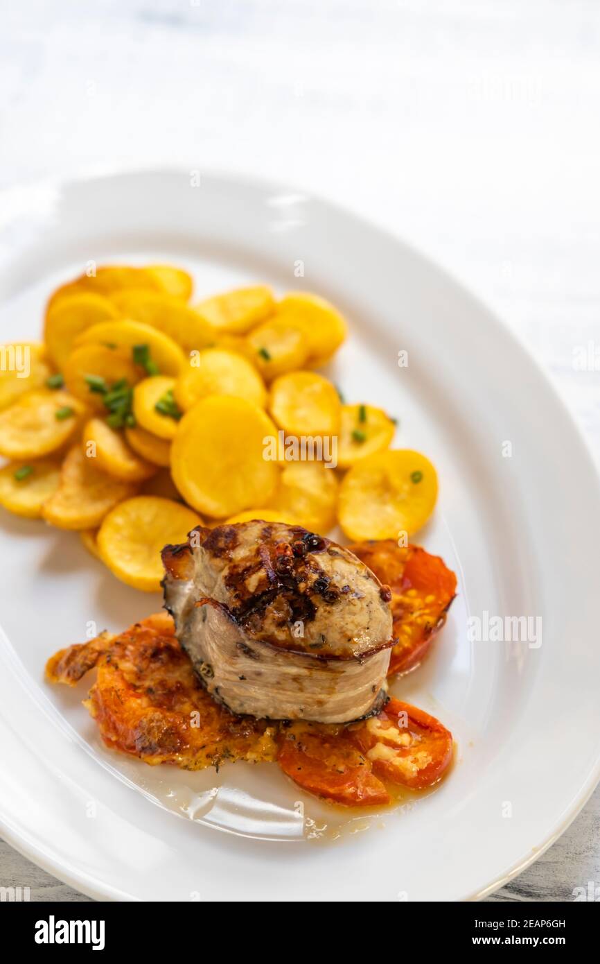 filetto di maiale in pancetta al pepe con patate e pomodori Foto Stock