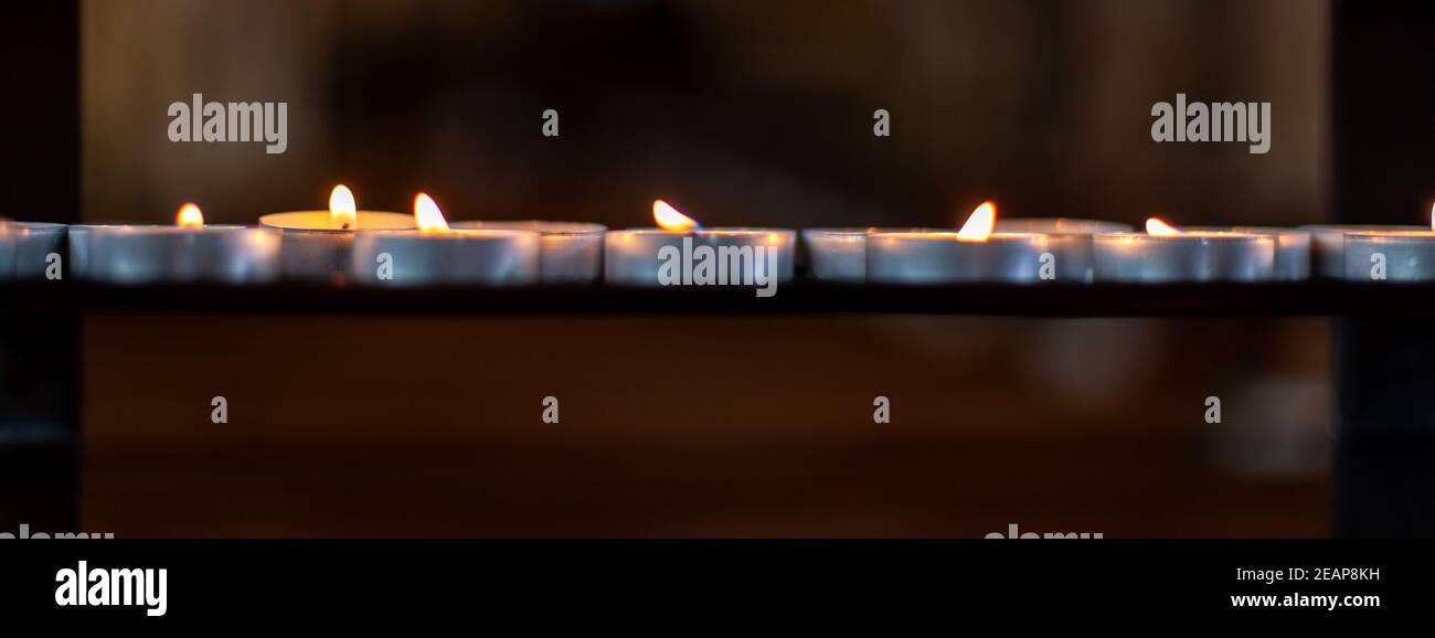 fila di candele che bruciano nella chiesa, banner Foto Stock