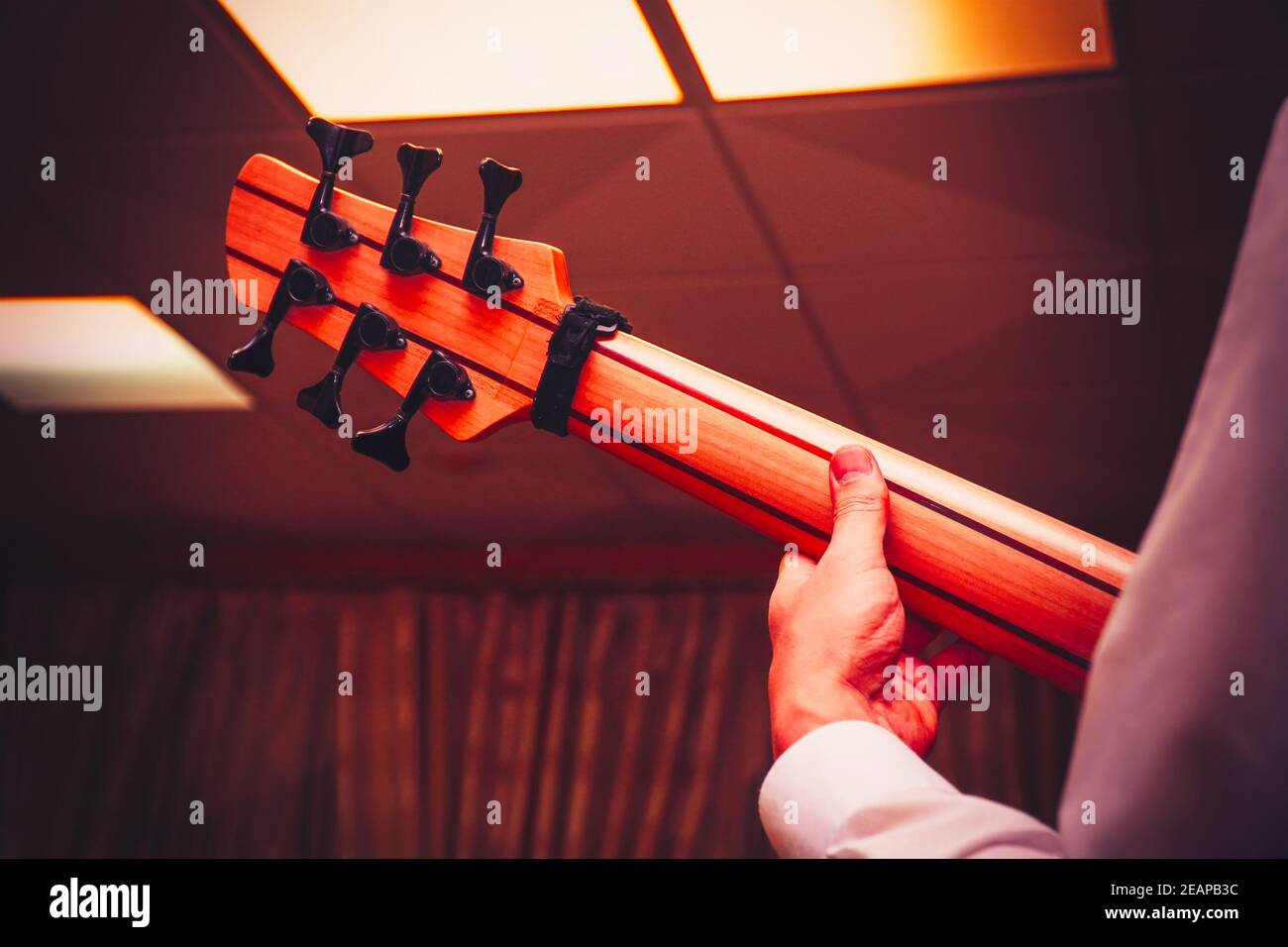 La mano del chitarrista sul collo di una chitarra basso a sei corde. Vista posteriore Foto Stock