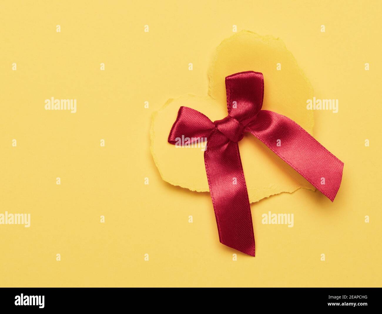 cuore di carta giallo e arco di seta rosso su sfondo giallo Foto Stock