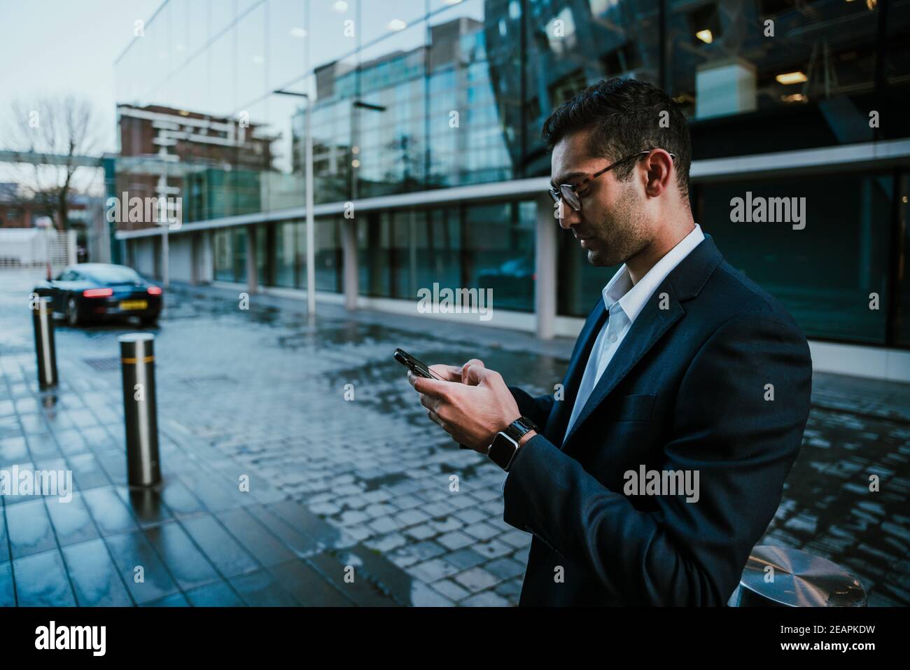 Corsa mista uomo d'affari chattando su smartphone a piedi per lavorare in edificio per uffici Foto Stock