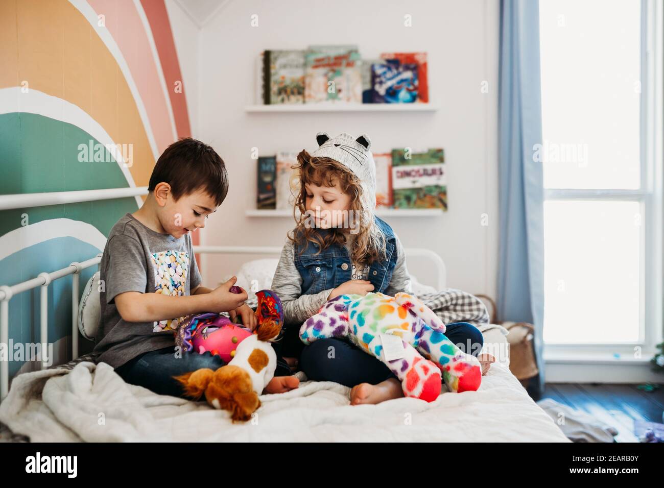 Fratello e sorella seduti sul letto nella camera dei bambini arcobaleno in riproduzione Foto Stock