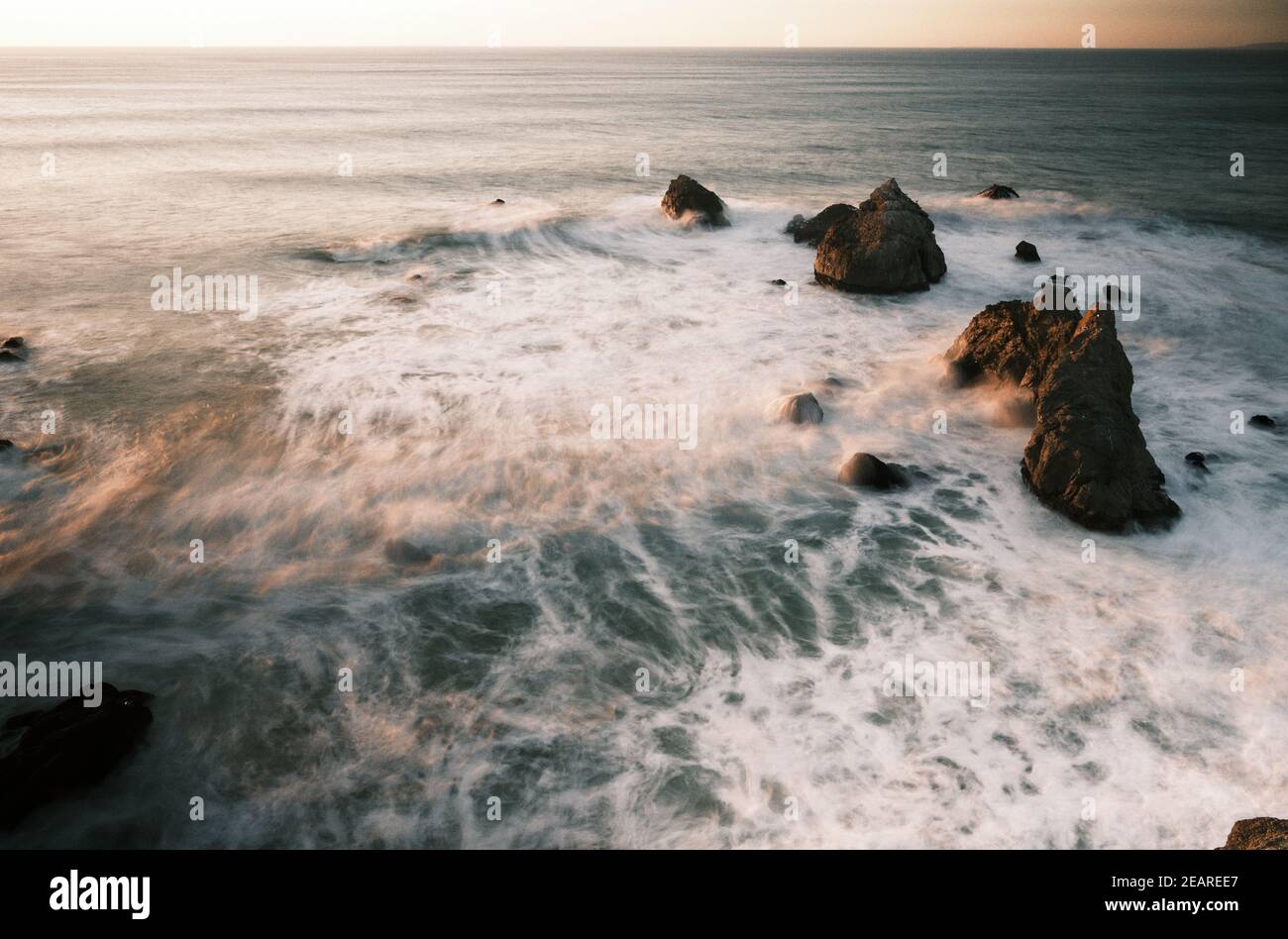Onde che scorrono tra le scogliere rocciose al tramonto Foto Stock