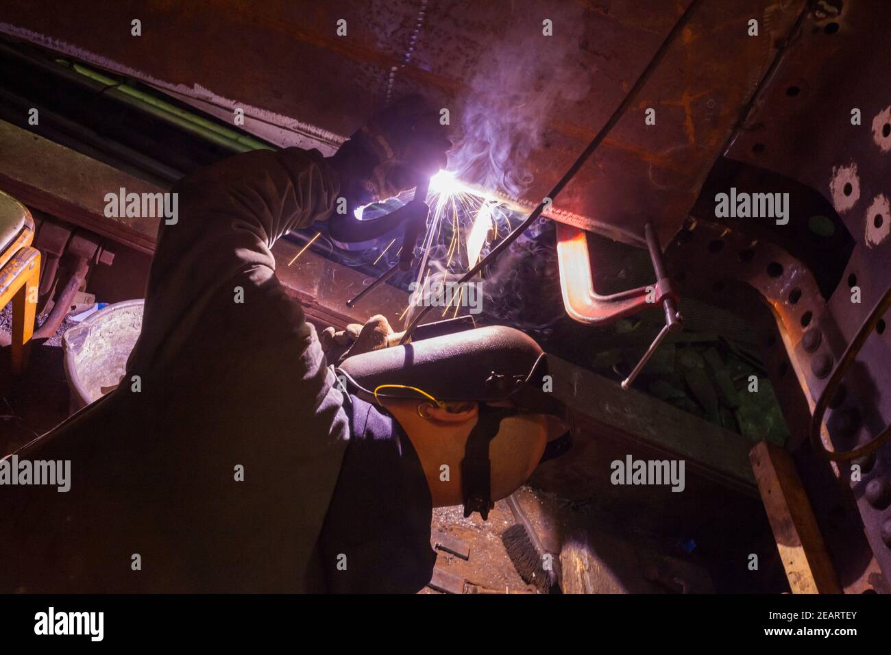 Saldatrice che lavora alla revisione di un vecchio vapore Locomotiva nel laboratorio della Valle di Keighley e Worth Ferrovia a Haworth Foto Stock