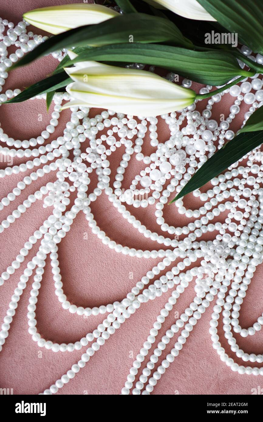 Gigli bianchi con foglie verdi e una collana di perle su sfondo rosa. Foto Stock