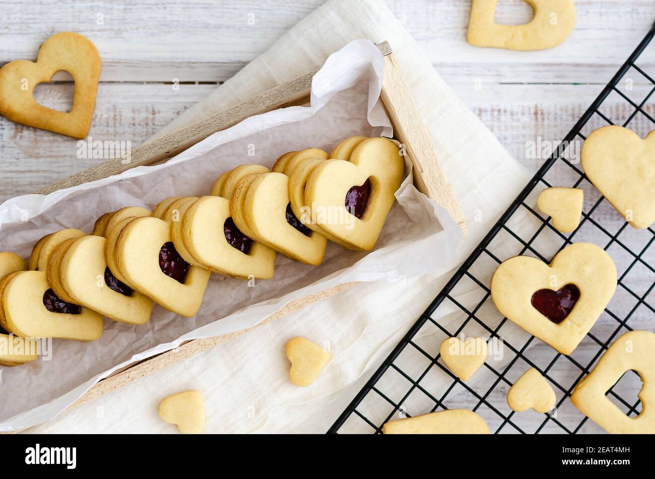 Biscotti a forma di cuore con confettura di lamponi e vaniglia in una scatola di legno e su una rastrelliera nera con un tovagliolo bianco. Foto Stock