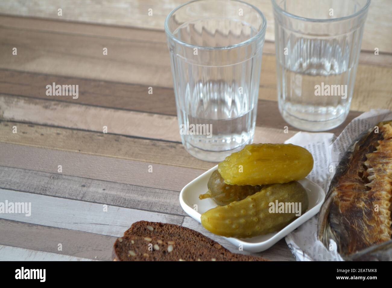 Colpo di vodka con uno stockfish e cetriolo sottaceto su un vecchio tavolo di legno. Foto Stock