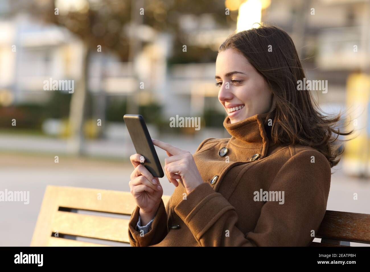 Donna felice in inverno con smartphone su una panca Foto Stock