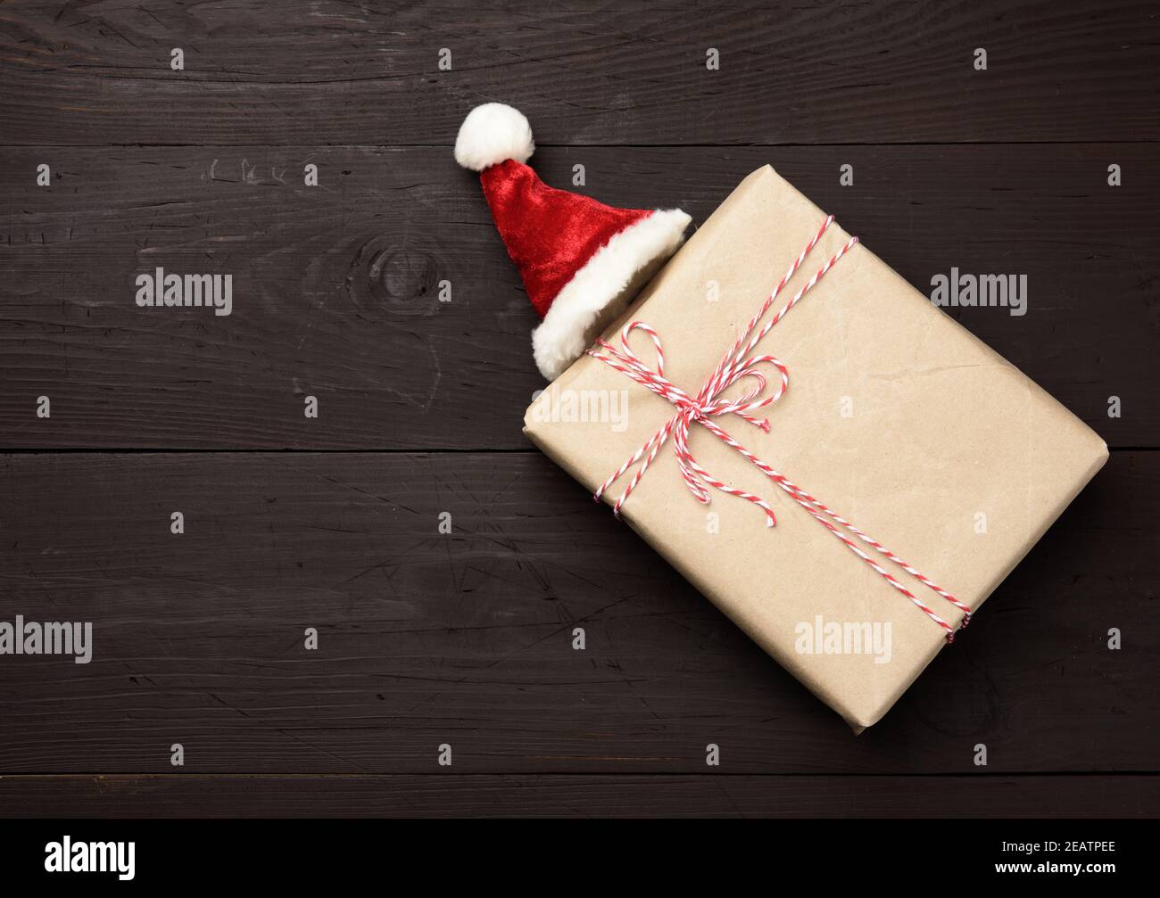 scatola quadrata avvolta in carta marrone kraft e cappuccio rosso, regalo su sfondo di legno Foto Stock