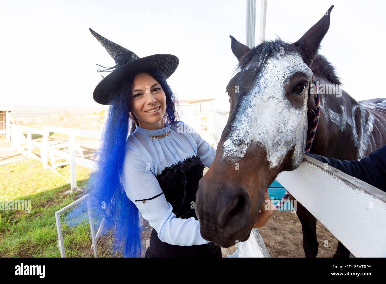 Una ragazza vestita da strega mostra il volto di un cavallo dipinto con vernice bianca per la vacanza di halloween Foto Stock
