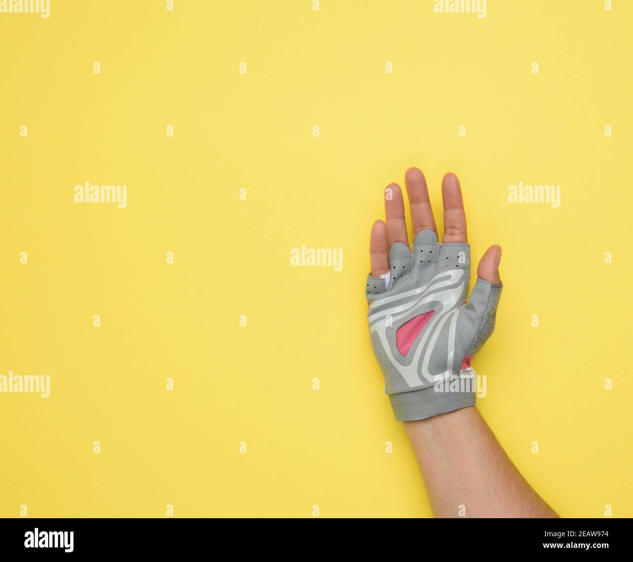 mano femminile in un guanto grigio per tributi allo sport e guidando una bicicletta su uno sfondo giallo Foto Stock