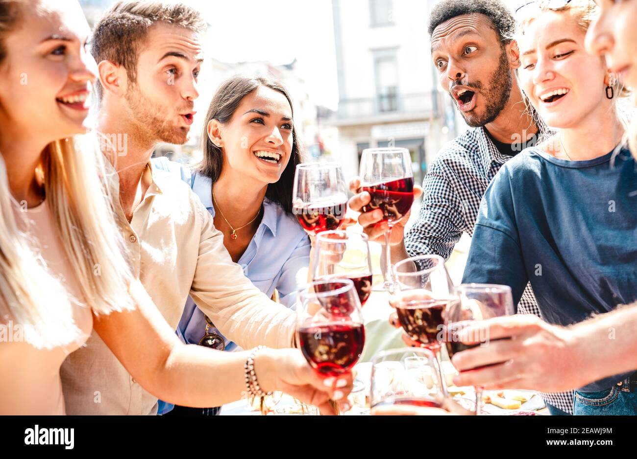 Felici amici multirazziali che si divertono a bere e tostare il vino rosso A pranzo festa - i giovani mangiano cibo barbecue a. ristorante cantina insieme Foto Stock