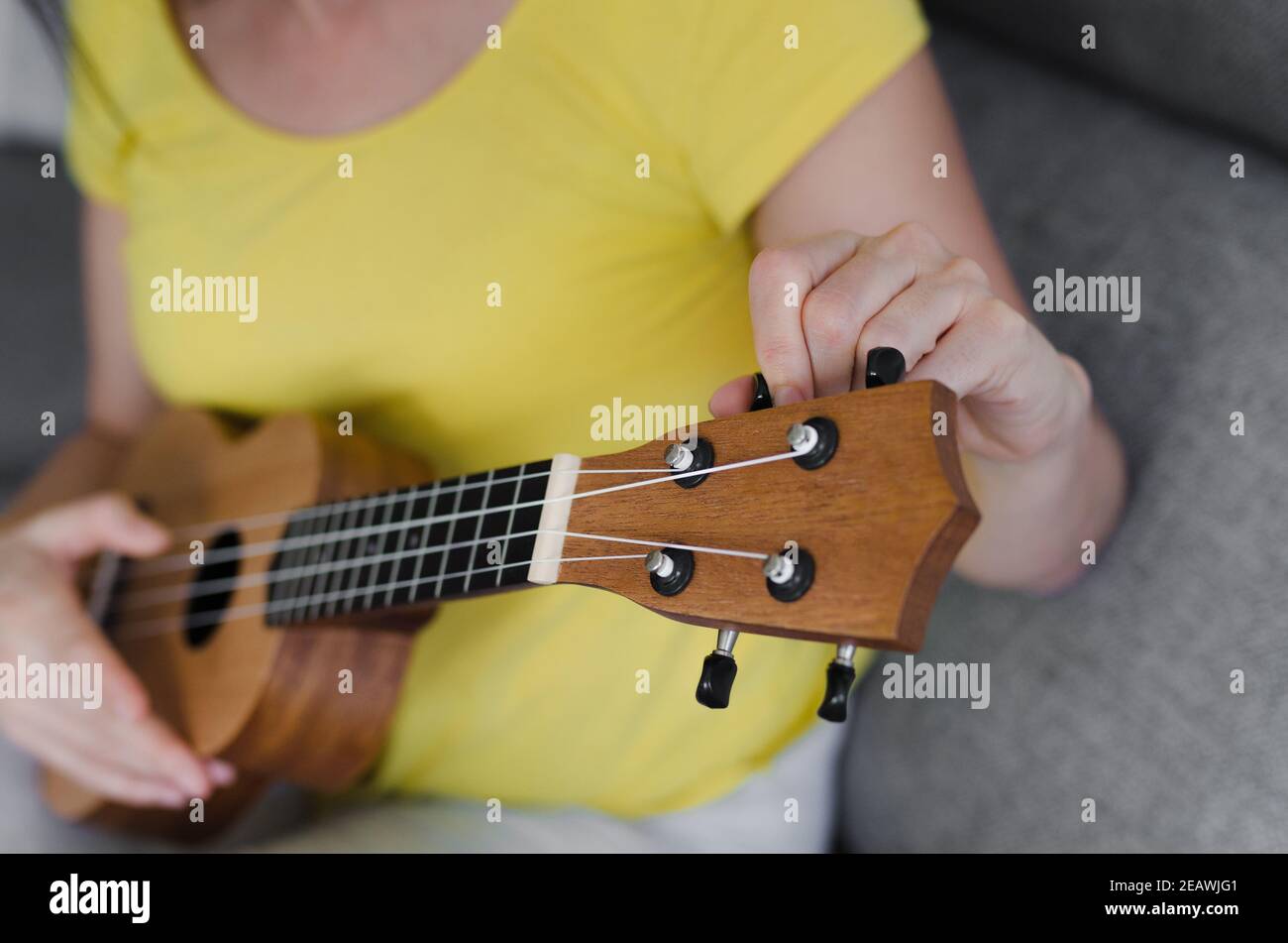primo piano di una donna irriconoscibile che sintonizza il suo ukulele. Sta sintonizzando il PEG della nota G. Foto Stock