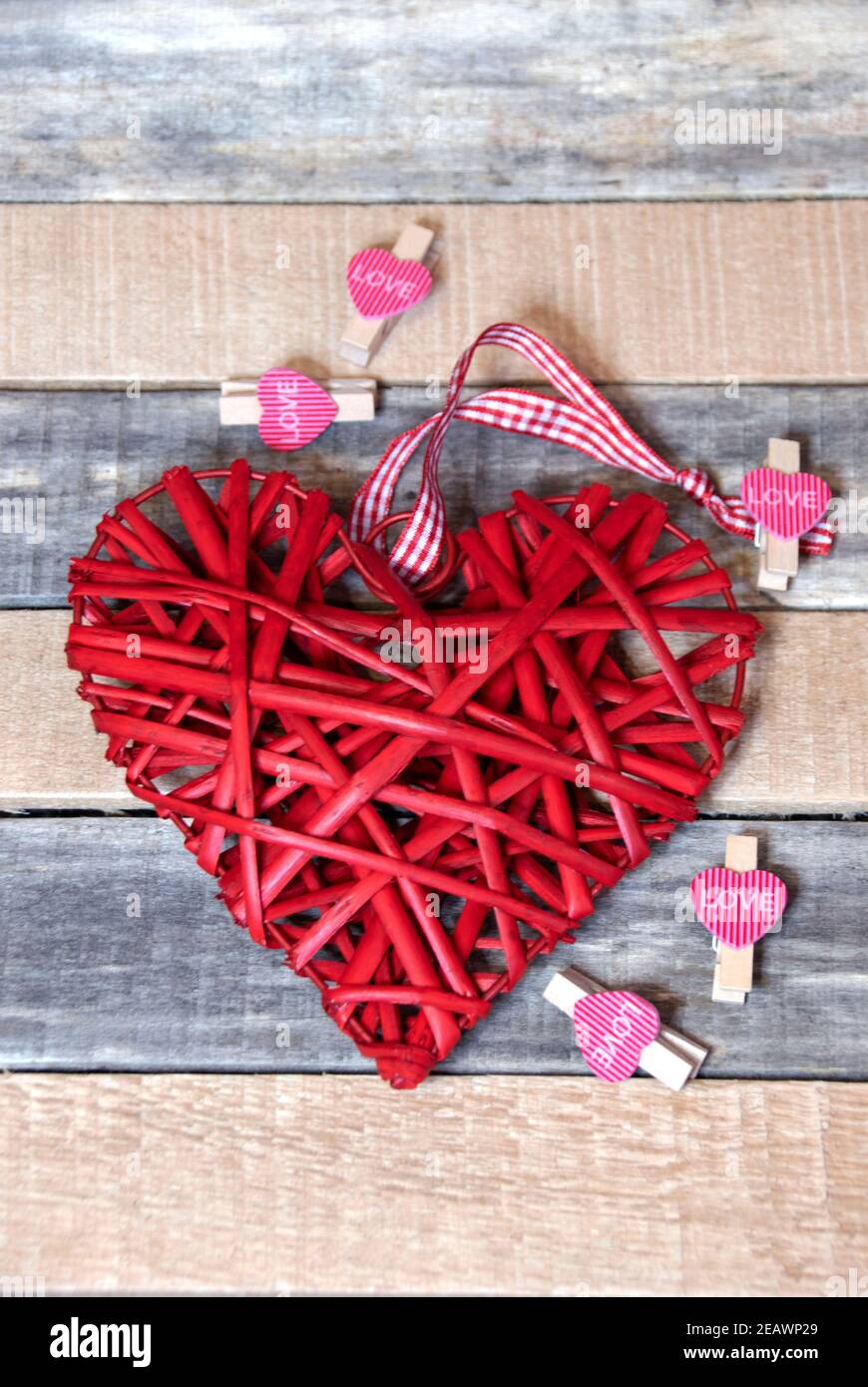 Cuori rossi e un grande cuore di paglia su uno sfondo di legno. Foto Stock