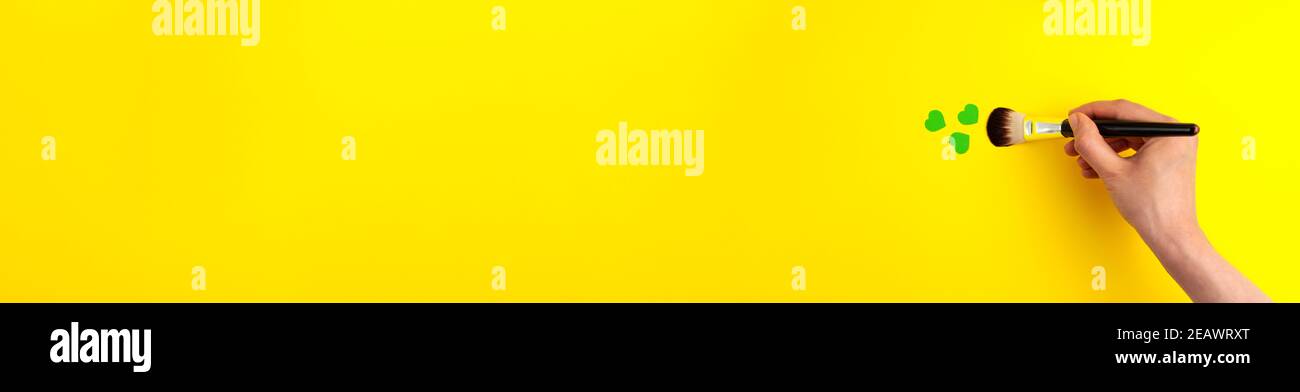 Banner piatto con vista dall'alto di cuori verdi e con pennello in mano a destra con spazio per la copia Su sfondo giallo giorno di San Patrizio 17 marzo t Foto Stock