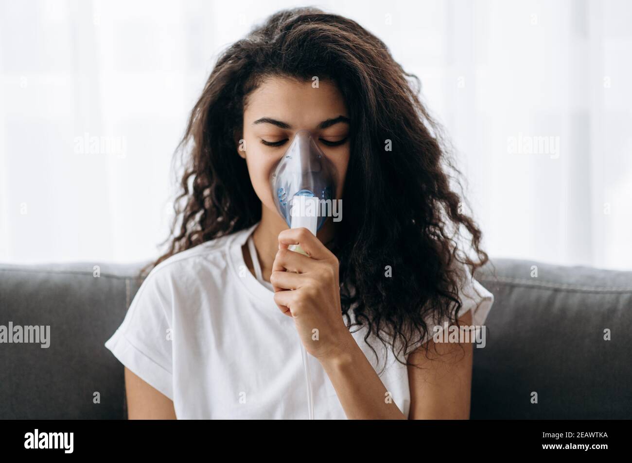 Foto ravvicinata di una donna afro-americana malata con un inalatore. Ragazza millenaria malsana che fa inalazione a casa, usa nebulizzatore e inalatore per t Foto Stock