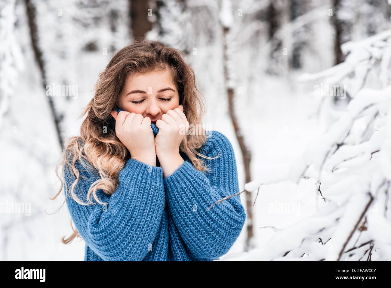 bella ragazza d'inverno in un pullover in maglia blu accogliente che gioca con neve Foto Stock