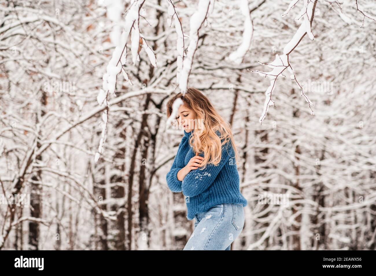 bella ragazza d'inverno in un pullover in maglia blu accogliente che gioca con neve Foto Stock