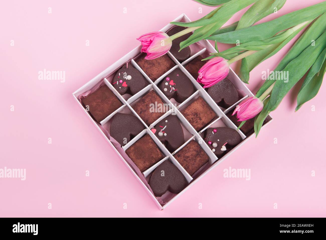 Confezione regalo con cuori di dolci al cioccolato e tulipani su sfondo rosa. Deserto per San Valentino Foto Stock