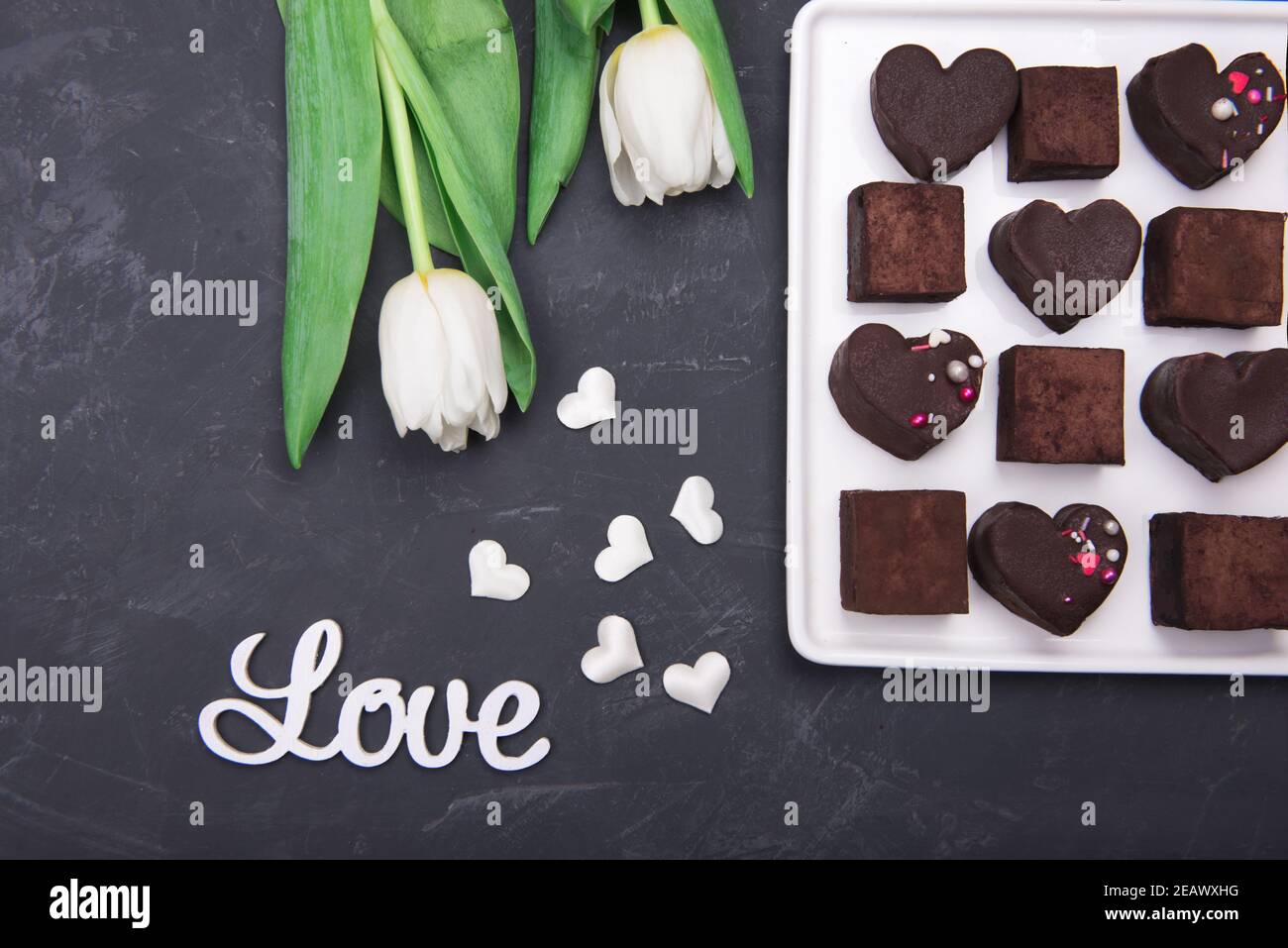 Confezione regalo con cuori di dolci al cioccolato e tulipani su sfondo scuro. Deserto per San Valentino Foto Stock