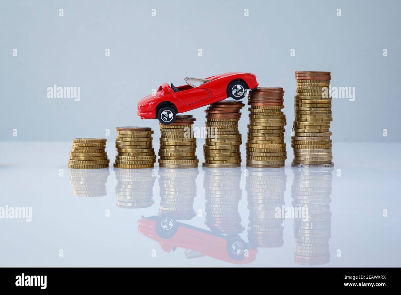 Auto giocattolo rossa su pile di monete ascendenti su sfondo grigio. Foto concettuale di prestito auto e finanza, risparmio di denaro per un'auto, assicurazione e investimento. Foto Stock