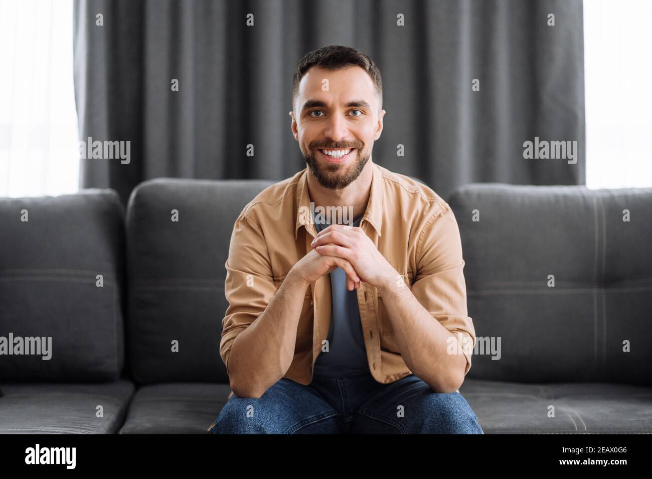Ritratto di un attraente ragazzo caucasico vestito in elegante abbigliamento casual. Uomo sicuro guarda direttamente la fotocamera con un sorriso amichevole mentre si siede Foto Stock