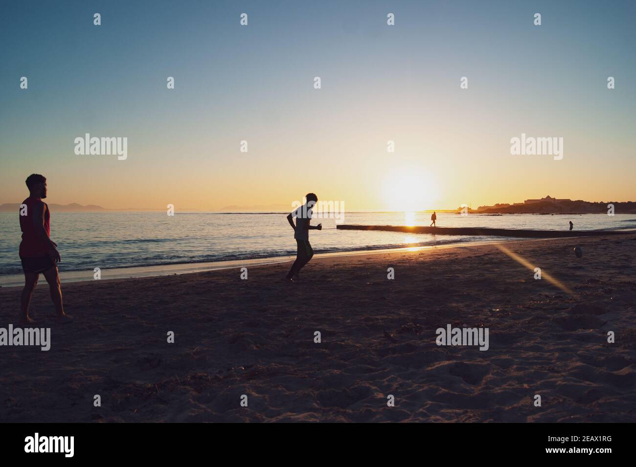 Giovani che giocano a rugby sulla spiaggia di Gordons Bay al tramonto Foto Stock
