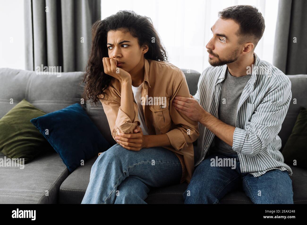 Coppia multirazziale in amore che litigano a casa sul divano sopra i problemi della famiglia o finanziari. La donna è offesa dall'uomo e lo ignora. Domesti Foto Stock