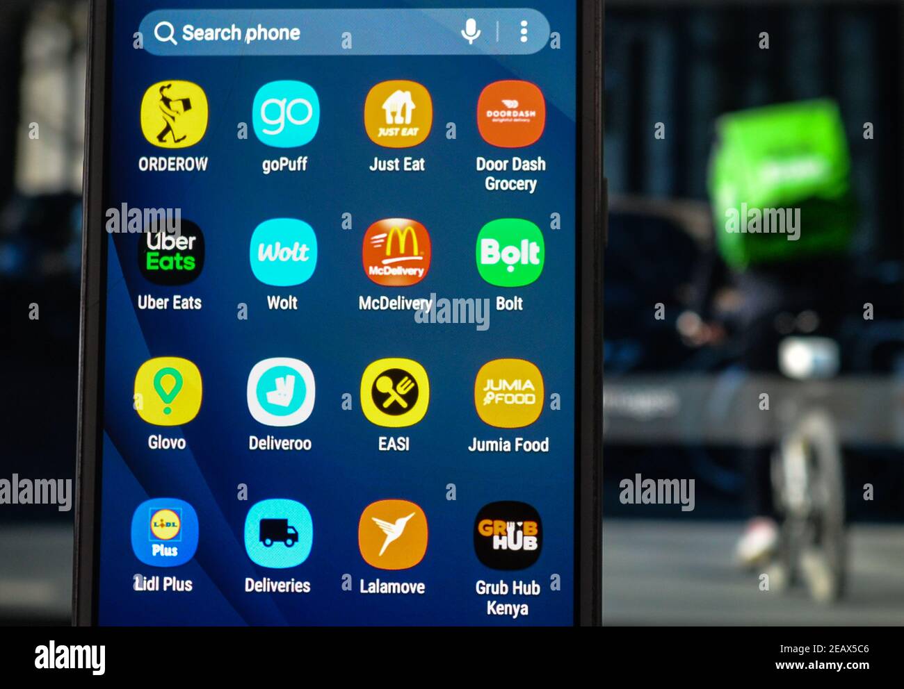 In questa illustrazione fotografica i loghi Orderow, goPuff, Just Eat, Door Dash, Uber Eats, Wolt, McDelivery, Bolt, Glovo, Deliveroo, EASI, Jumia Food, Lidl Plus, Deliveries, Lalamove e GRUB Hub vengono visualizzati sullo schermo di un telefono cellulare con l'immagine di un corriere per la consegna di cibo visualizzato sullo schermo di un computer. Foto Stock