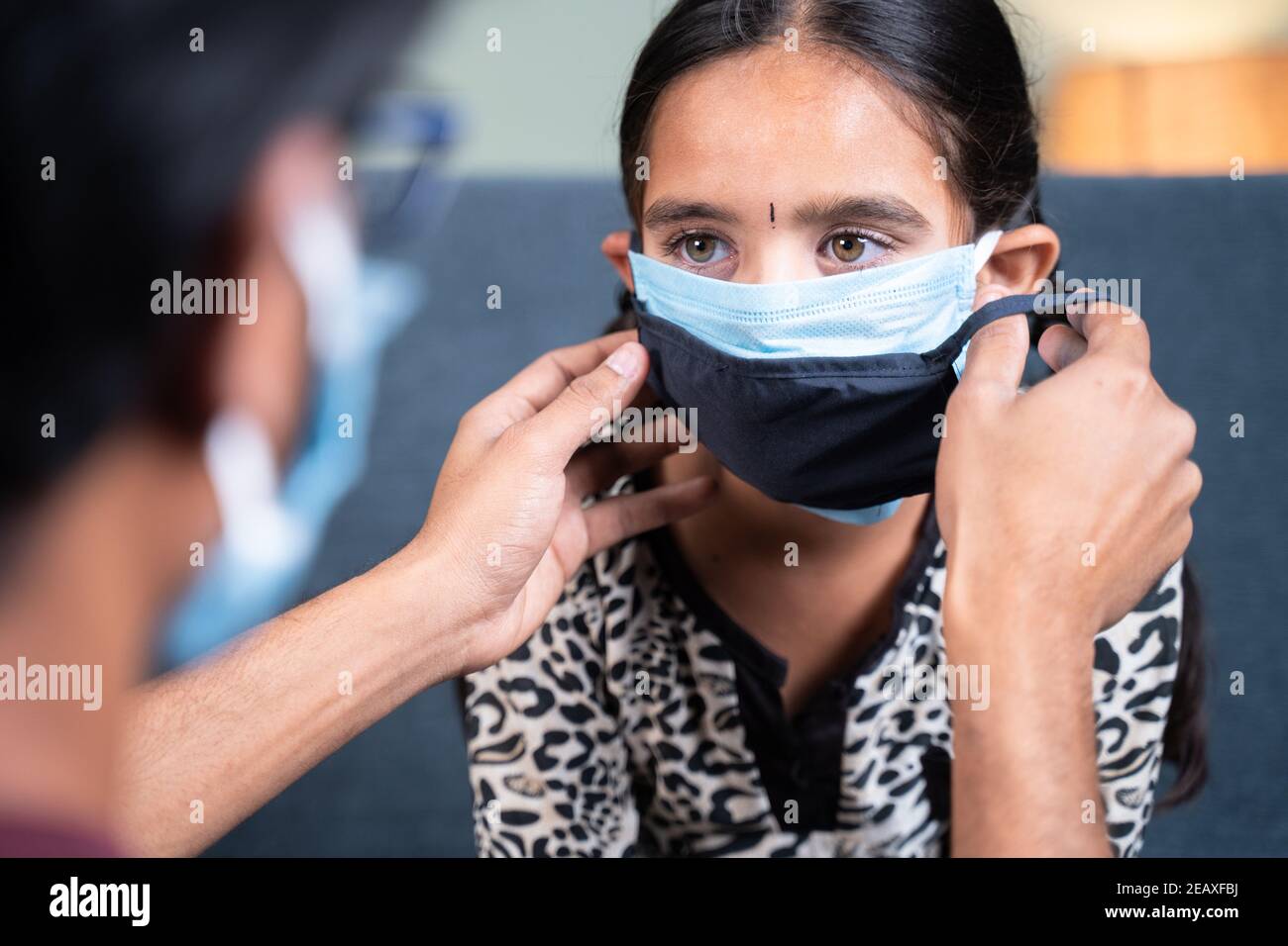 Spalla colpo di padre che aiuta sua figlia a indossare doppia o due maschera viso a casa per proteggere da coronavirus covid-19 pandemia prima di uscire. Foto Stock