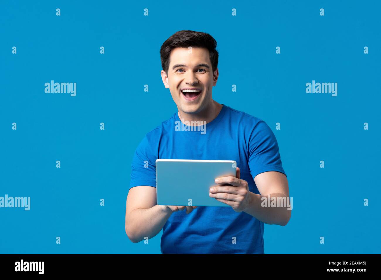 Felice uomo americano che si diverte a navigare in internet con il suo computer tablet isolato su sfondo blu dello studio Foto Stock