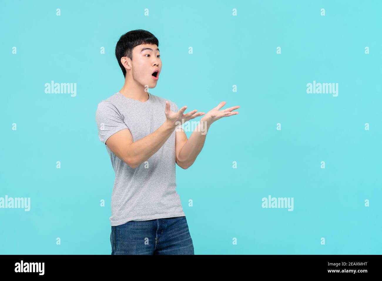Uomo asiatico alzando le mani con faccia scioccata guardando vuoto spazio da parte isolato su sfondo blu chiaro studio Foto Stock