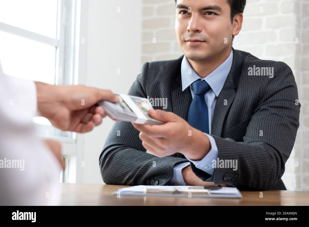 Uomo d'affari ispanico che consegna denaro al partner dopo aver firmato il prestito contratto Foto Stock