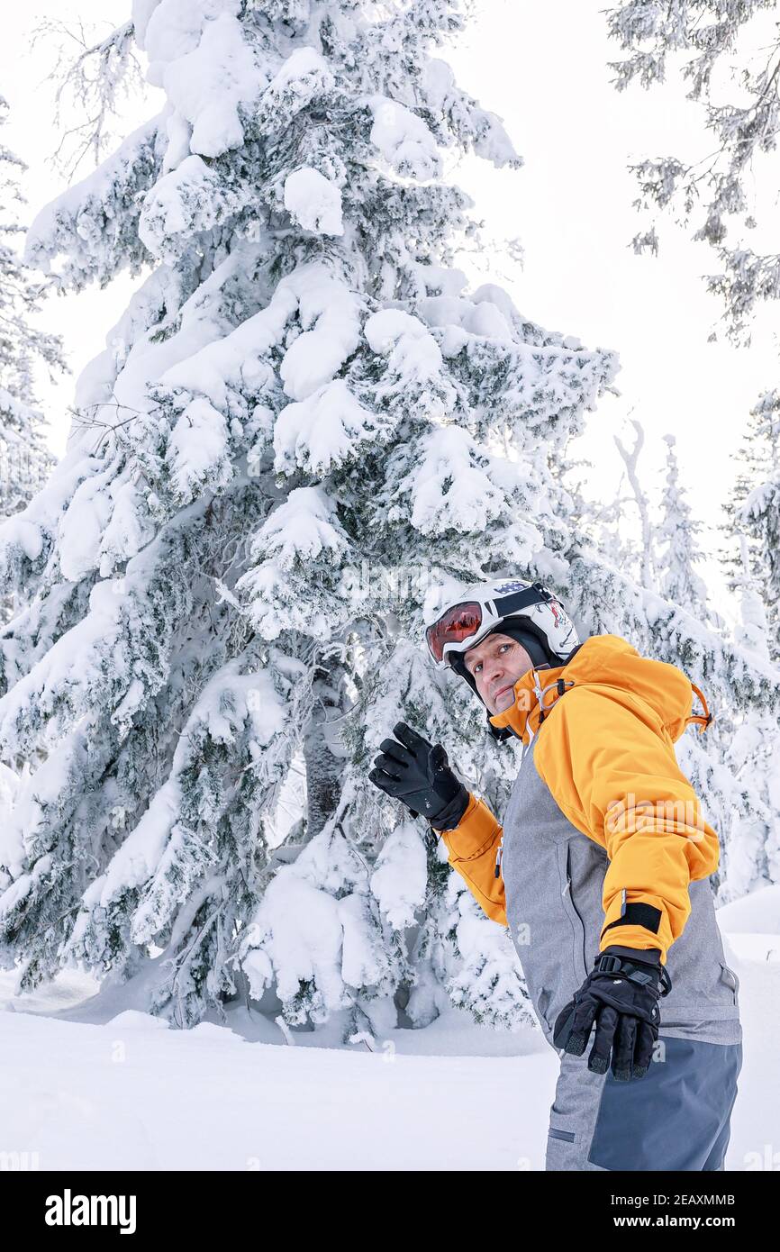 Happy snowboarder maschile in tuta luminosa in un casco sportivo e occhiali da sci sullo sfondo di una foresta innevata. Sport estremi. Vacanze attive. Foto Stock