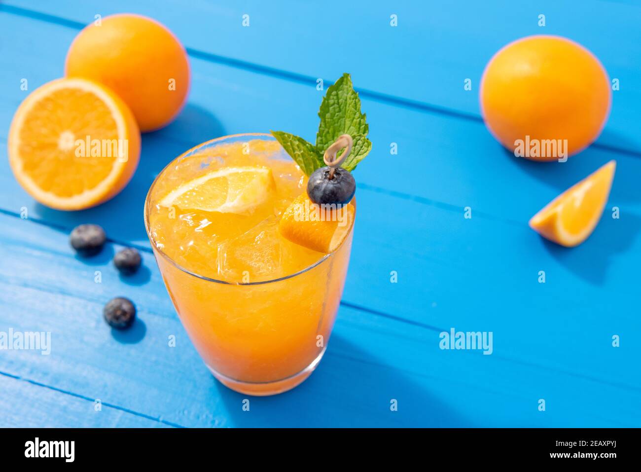 Succo di frutta fresca mocktail bevande nei bicchieri con arance e mirtilli su colorato tavolo blu Foto Stock