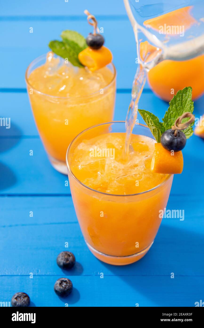 Rinfrescanti cocktail di succo d'arancia cocktail estivo nei bicchieri con cubetti di ghiaccio su colorato sfondo blu tavola di legno Foto Stock
