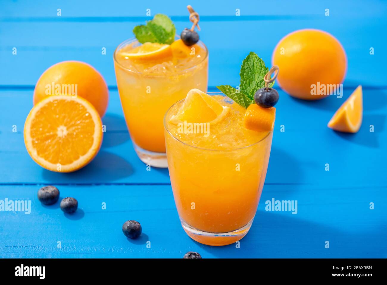 Spremute fresche di frutta spremuta bevande nei bicchieri con arance e mirtilli sul tavolo blu Foto Stock
