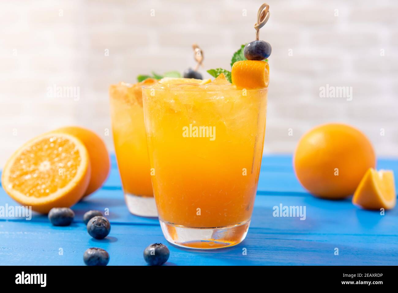 Variopinto succo di frutta fresca, mocktail drink con arance e mirtilli su sfondo blu della tabella Foto Stock