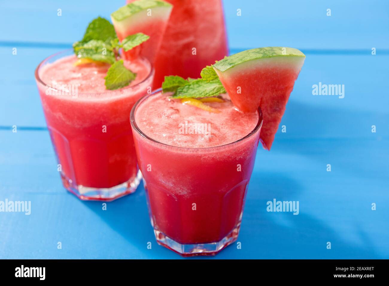 Succo di anguria bevande estive nei bicchieri con fette di foglie di frutta e menta usate per guarnire su tavola blu Foto Stock