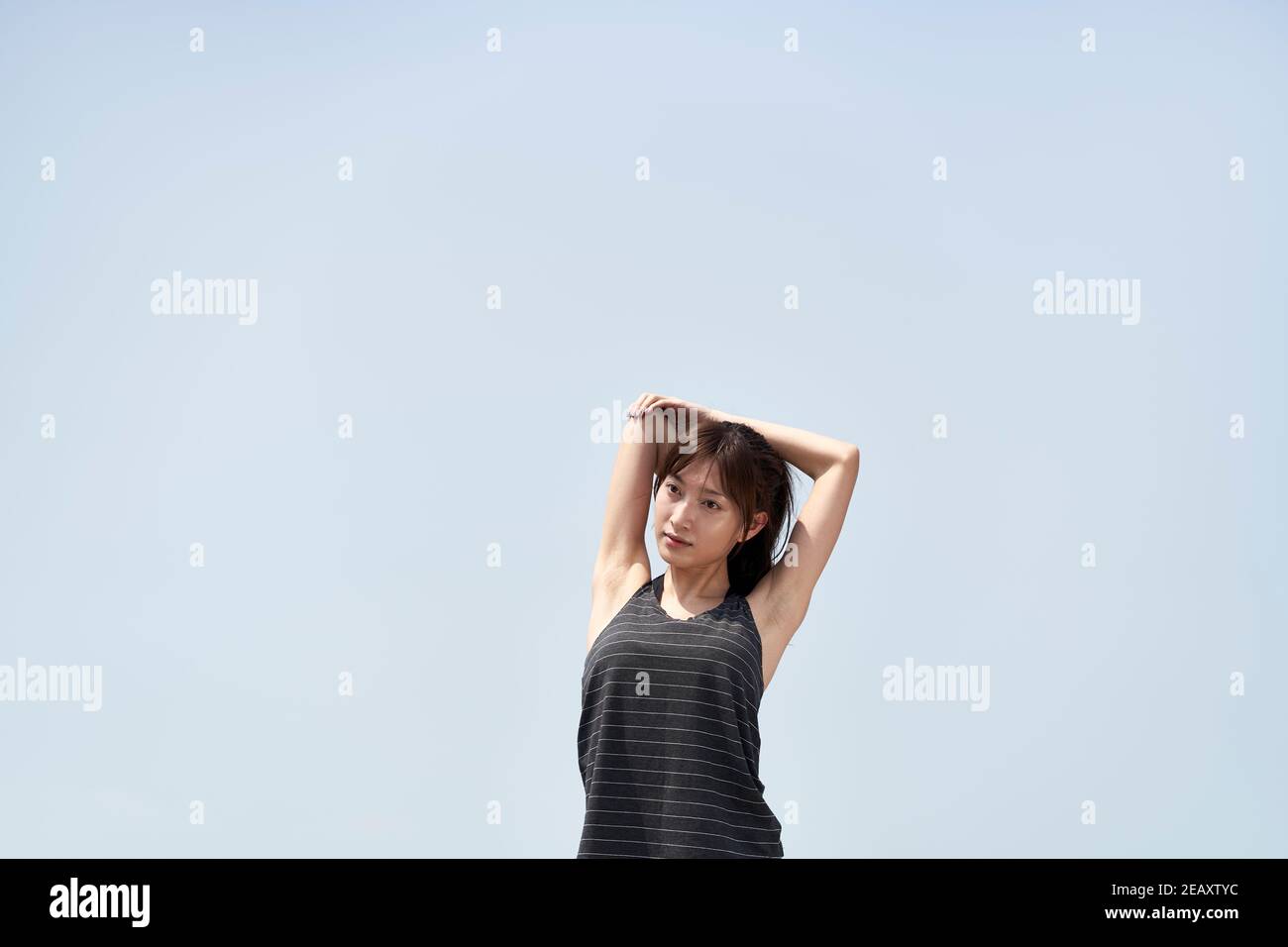 giovane donna asiatica in sportswear che allunga le braccia all'aperto contro il blu cielo Foto Stock
