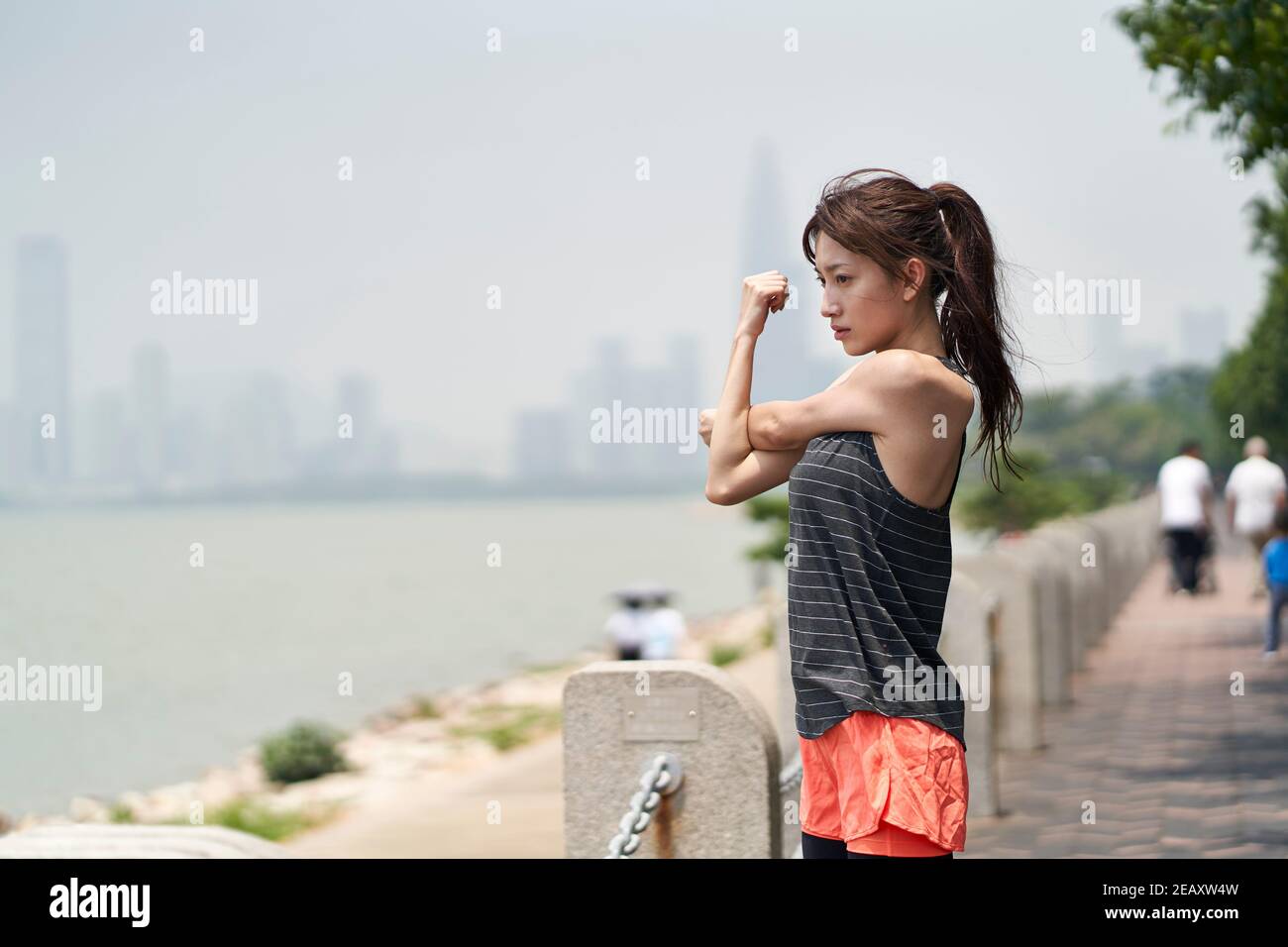 giovane donna asiatica in abbigliamento sportivo che si riscalda prima di allenarsi all'aperto nel parco sul mare Foto Stock