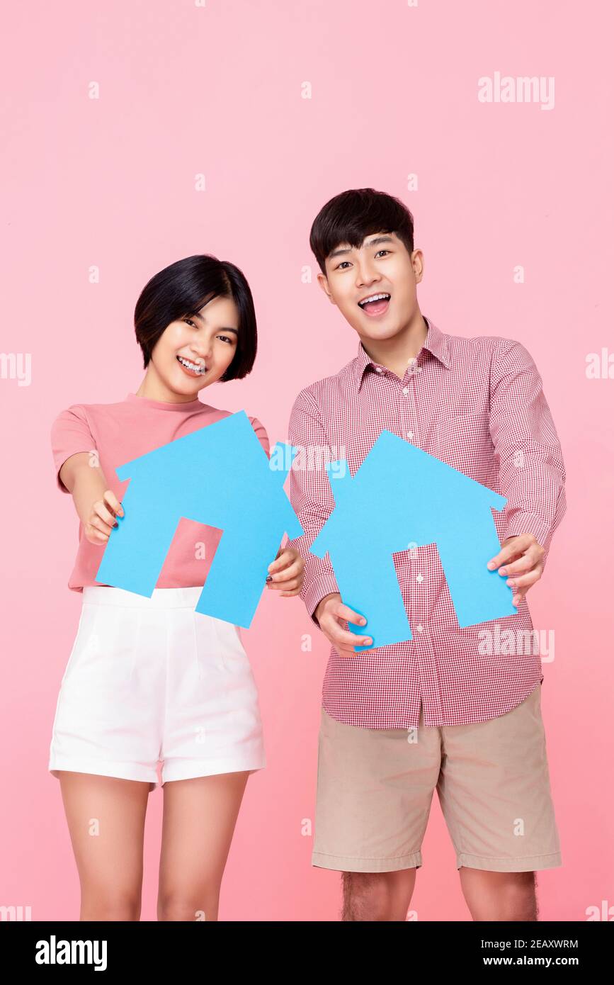 Giovane felice coppia asiatica che presenta i simboli di casa in sfondo di studio rosa per il concetto di prestito domestico finanziario Foto Stock