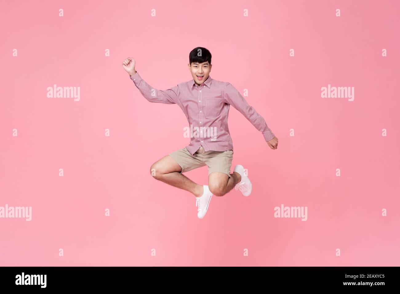 Energico felice sorridente giovane asiatico in abiti casual salto studio girato isolato in colorato sfondo rosa Foto Stock