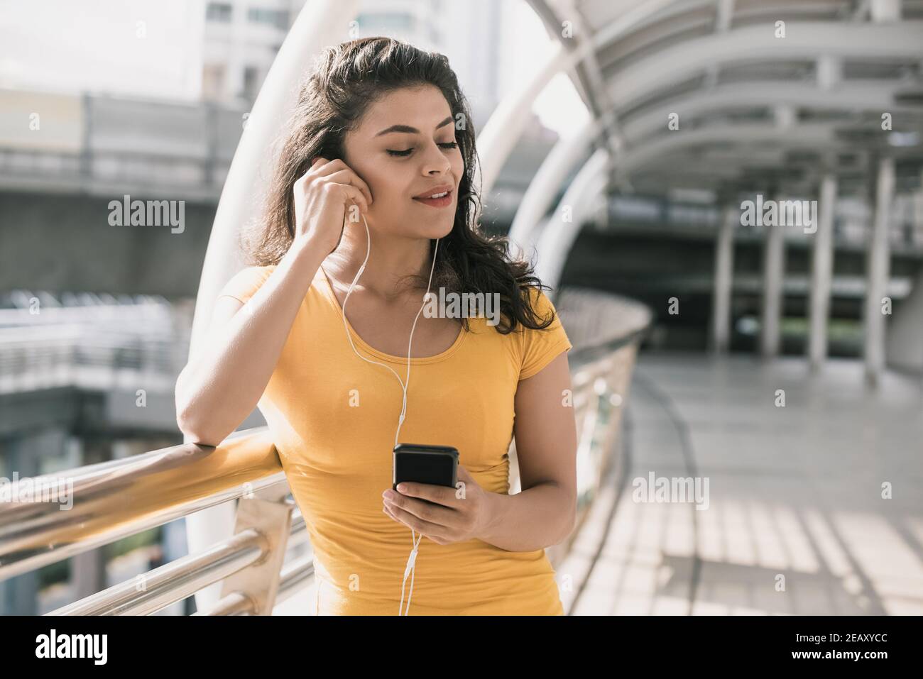 Giovane donna ispanica che indossa le cuffie per ascoltare la musica con gli occhi chiuso nel passaggio coperto della città Foto Stock