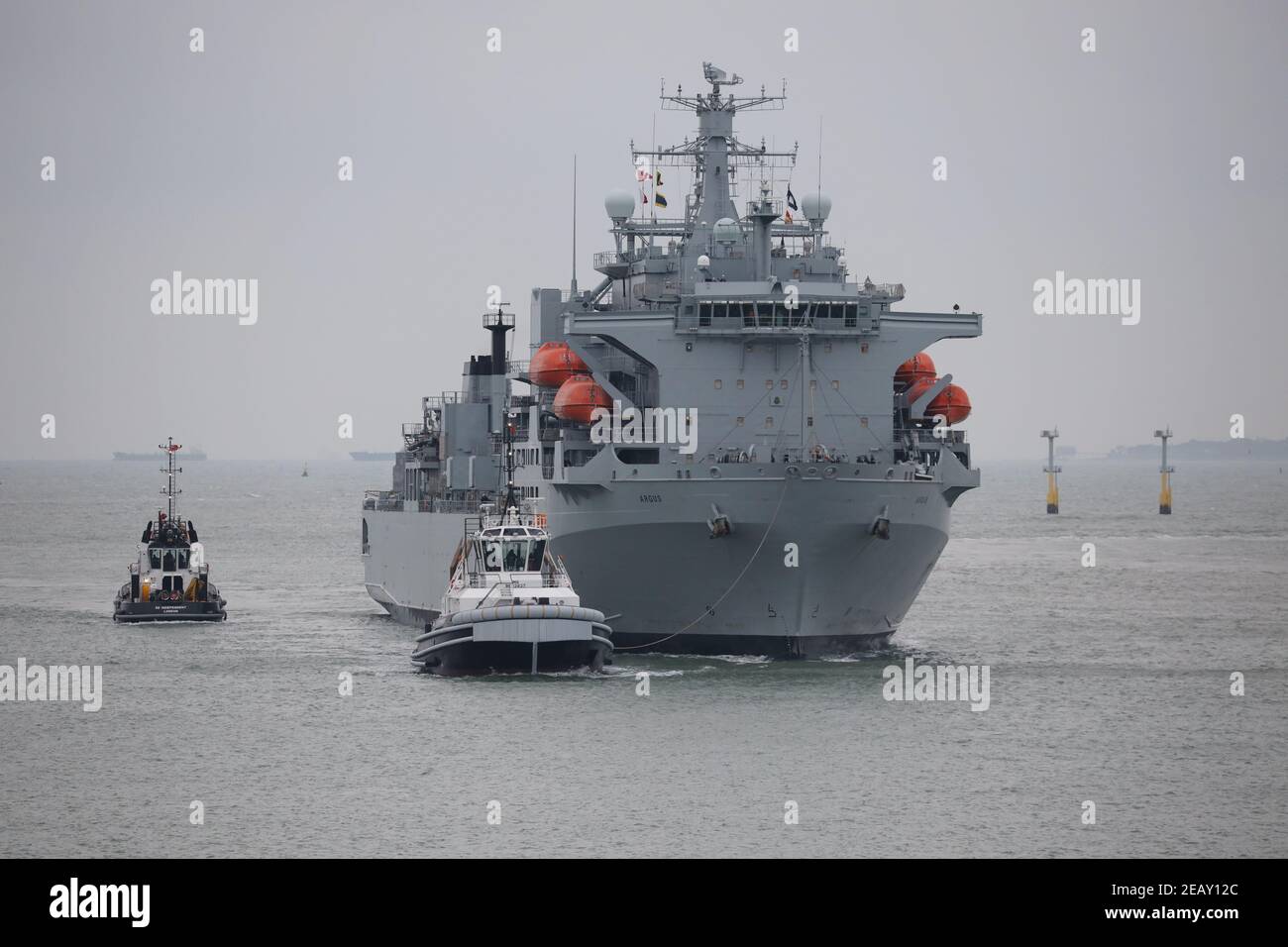 Tugs scortano la Royal Fleet Auxiliary nave ARGUS come esso Arriva alla base navale la mattina presto Foto Stock