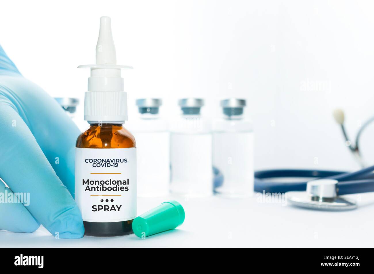 Il medico tiene una fiala di anticorpi monoclonali spray nasale, un nuovo trattamento per Coronavirus Covid-19, su un tavolo bianco con alcuni flaconcini e uno stetoscopio Foto Stock