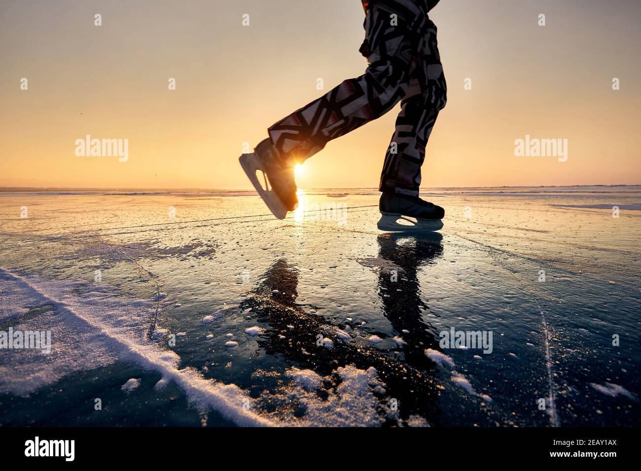 Primo piano gambe di uomo con pattinaggio su ghiaccio in silhouette al lago ghiacciato contro la bella alba arancione Foto Stock