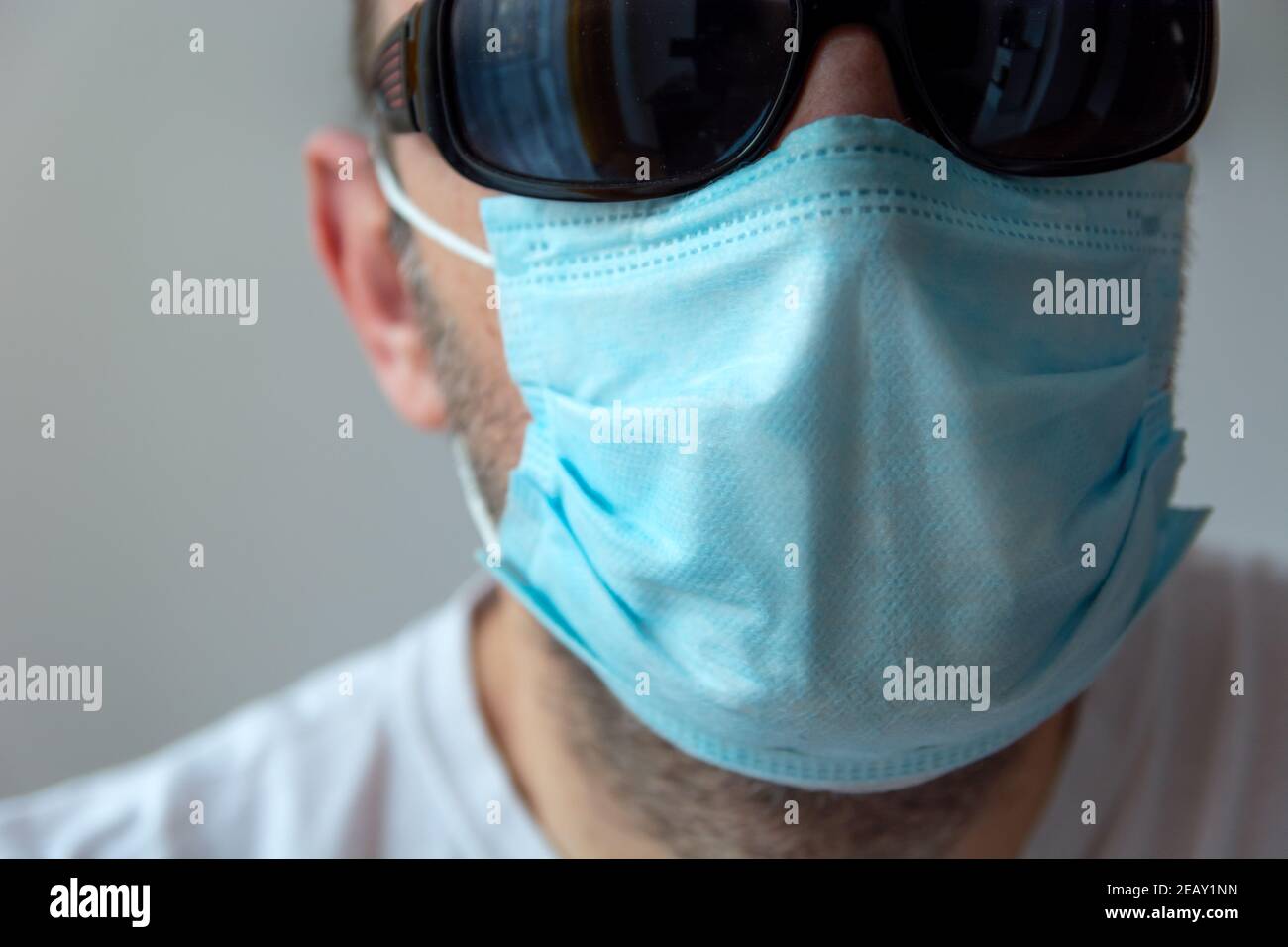 Faccia maschile in una maschera chirurgica blu e occhiali da sole neri Foto Stock