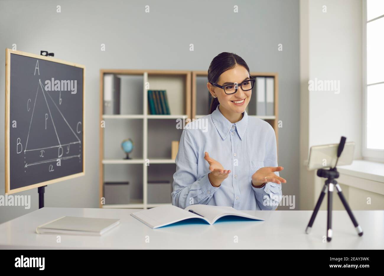 Giovane insegnante di scuola che dà lezioni di geometria online, utilizzando smartphone con treppiede Foto Stock