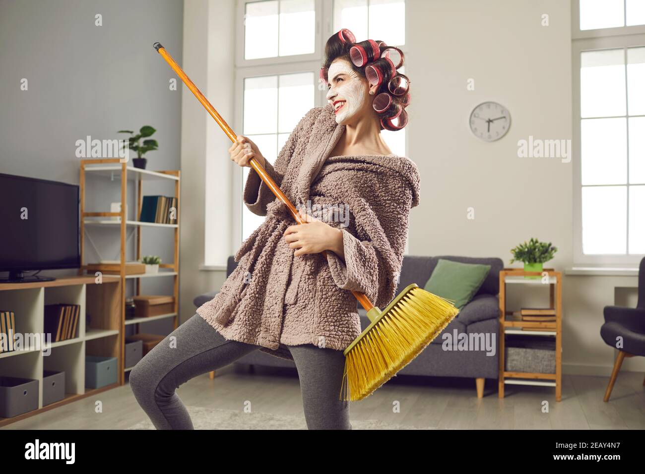 Felice giovane casalinga che suona sulla chitarra MOP e si diverte mentre pulisce la sua casa Foto Stock